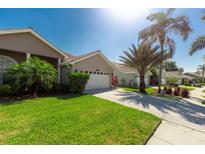 Charming home featuring a well-manicured lawn, lush tropical plants, and a spacious driveway to the two-car garage at 1729 Arabian Ln, Palm Harbor, FL 34685
