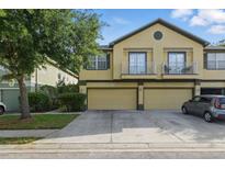 Two-story tan townhome featuring dual car garages, a small balcony, and verdant landscaping at 27563 Pleasure Ride Loop, Wesley Chapel, FL 33544