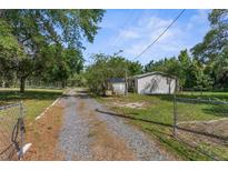 Quaint single-story home featuring a gravel driveway leading to a cozy residence, surrounded by lush greenery and trees at 3373 Olson Rd, Spring Hill, FL 34607