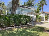 Charming light blue home with white trim, elevated deck and lush landscaping, offering a serene tropical feel at 401 Pennsylvania Ave, Crystal Beach, FL 34681
