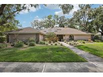 Charming single-story home with a well-manicured lawn, mature trees, and solar panels on the roof at 10902 Bent Tree Pl, Tampa, FL 33618
