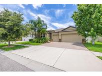 Charming single-Gathering home featuring a manicured lawn, mature trees, and a two-car garage with brick-paved driveway at 9860 Smarty Jones Dr, Ruskin, FL 33573