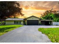 Charming single-story home with a welcoming driveway, lush lawn, and well-manicured landscaping under a beautiful sunset at 7211 Red Oak Loop, New Port Richey, FL 34654