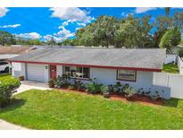 Charming single-story home featuring a well-manicured lawn, gray roof, and colorful landscaping at 1809 Chinaberry Dr, Oldsmar, FL 34677