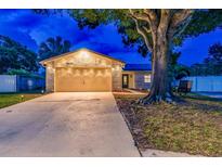 Charming single-story home featuring a large tree, a two-car garage, and warm string lights illuminating the front at 1910 Montego Ct, Oldsmar, FL 34677