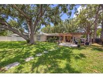 Expansive backyard features mature trees, a stone pathway, patio with pergola and outdoor seating at 10730 52Nd N Ave, St Petersburg, FL 33708