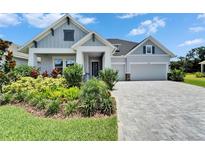 Charming, modern home featuring a well-manicured lawn, a brick driveway, and an attached two-car garage at 5971 Hidden Branch Dr, Apollo Beach, FL 33572