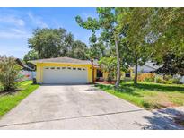 Charming, yellow single-story home featuring a spacious front yard, a two-car garage, and lush, mature landscaping at 1510 Patricia Ave, Dunedin, FL 34698