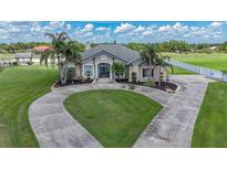 Elegant home with a circular driveway, lush lawn, mature palm trees and landscaped garden beds at 7301 Loghouse Rd, Plant City, FL 33565