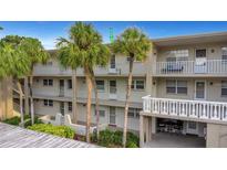 Three-story condo building with palm trees, white railings, and balconies with a peek of an outdoor dining area at 940 Virginia St # 303, Dunedin, FL 34698