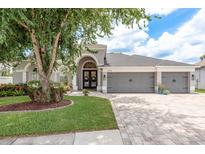 Charming single-story home featuring a well-manicured lawn, gray garage doors, and a brick-paved driveway at 16226 Carnoustie Dr, Odessa, FL 33556