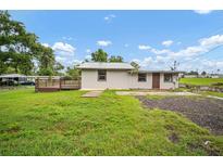 View of home from backyard, featuring a wood deck, green lawn, and cloudy blue skies at 37732 Cecil Ln, Zephyrhills, FL 33542