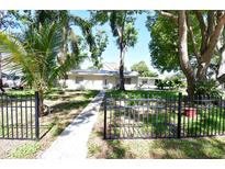Charming home featuring a manicured lawn, mature trees, and black metal decorative fencing at 7684 Oakhurst Rd, Seminole, FL 33776