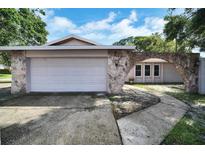 Charming home featuring a stone archway and a two-car garage with a white door, enhancing its curb appeal at 2817 Rustic Oaks Dr, Palm Harbor, FL 34684