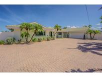 Charming single-story home with a brick driveway, attached garage, and well-maintained landscaping with palms at 5950 Bikini N Way, St Pete Beach, FL 33706