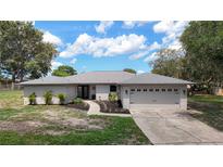 Charming single-story home featuring manicured landscaping, a two-car garage, and a welcoming entrance under a partly cloudy sky at 7511 Laurel Oak Ct, Port Richey, FL 34668