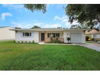 Charming single-story home featuring a manicured lawn, front porch, and attached garage in a quiet neighborhood at 245 Grove Cir N, Dunedin, FL 34698