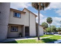 Condo exterior featuring a tan facade, green lawn and mature palm trees set against a blue sky with white clouds at 6338 Newtown Cir # 38A6, Tampa, FL 33615