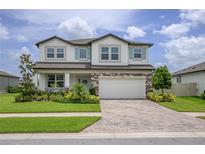 Charming two-story home featuring a brick-accented facade, paver driveway, manicured lawn, and bright blue window shutters at 12189 Nouveau Ave, Spring Hill, FL 34610