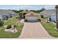 Charming single-story home featuring a brick paver driveway and well-manicured lawn, surrounded by lush landscaping at 1901 E Del Webb Blvd, Sun City Center, FL 33573