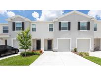 Charming townhomes with well-manicured lawns and attached garages under a cloudy blue sky at 33063 Tulip Petal Ln, Wesley Chapel, FL 33545