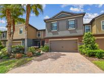 Charming townhome featuring lush landscaping, a brick driveway, and a two-car garage at 28568 Tranquil Lake Cir, Wesley Chapel, FL 33543