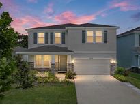 Charming two-story home featuring a well-manicured lawn, stone accents, gray exterior, and an attached two-car garage at 13735 Wineberry Dr, Dade City, FL 33525