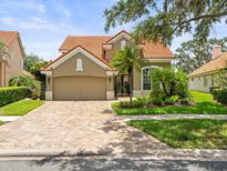 Charming single-Gathering home featuring a tile roof, lush landscaping, and a brick paved driveway at 18917 Avenue Biarritz, Lutz, FL 33558
