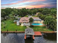 Waterfront home featuring a private pool, dock, and lush landscaping against a colorful sunset backdrop at 2401 Roberta Ln, Clearwater, FL 33764