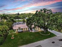 Beautiful home exterior features a large front yard, mature trees, and a screened-in pool at 2401 Roberta Ln, Clearwater, FL 33764
