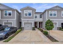 Gray townhome featuring a gray garage door, well-maintained landscaping, and a concrete driveway at 5813 Grand Sonata Ave, Lutz, FL 33558