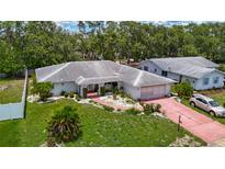 Inviting single-Gathering home featuring lush landscaping, a red brick driveway, and mature trees surrounding the property at 1607 New Bedford Dr, Sun City Center, FL 33573