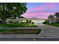 Charming single-story home featuring a well-manicured lawn, mature trees, and a two-car garage under a pastel sky at 2418 Cardwell Way, Sarasota, FL 34231