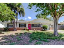 Charming single-story home with a pink front door, white exterior, brick accents and beautiful mature trees at 565 55Th Ne Ave, St Petersburg, FL 33703