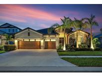 Charming home featuring a manicured lawn and a three-car garage, beautifully illuminated at dusk at 14514 Woodland Spur Dr, Lithia, FL 33547