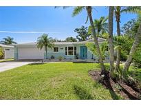 Charming, single-story home with a well-manicured lawn, palm trees, and bright blue front door at 709 Pinewood Dr, Dunedin, FL 34698