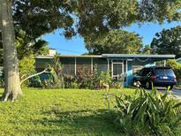 Charming single story home featuring lush landscaping, screened porch and driveway with parked car at 1605 Logan St, Clearwater, FL 33755