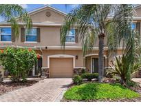 Charming townhome with a one-car garage, brick driveway, and lush landscaping at 26835 Juniper Bay Dr, Wesley Chapel, FL 33544