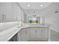 Modern kitchen featuring white cabinets, gold hardware, marble countertops and a view to the outside at 5430 Eagles Point Cir # 202, Sarasota, FL 34231