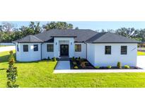 An attractive single-story home features a white exterior, dark roof, manicured lawn, and a welcoming entry at 14080 Sydney Rd, Dover, FL 33527