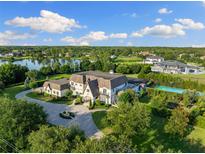 Expansive aerial view of an estate home with lush landscaping, a lake, and a tennis court under a bright blue sky at 18521 Wayne Rd, Odessa, FL 33556