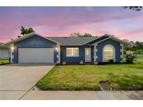 Charming single-story home featuring a well-manicured lawn, blue exterior, and a two-car garage at 8823 Aruba Ln, Port Richey, FL 34668
