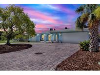 Charming blue home with a paver driveway and lush landscaping under a vivid, colorful sky at twilight at 304 Westwinds Dr, Palm Harbor, FL 34683