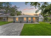 Charming single-story home with gray exterior, well-manicured lawn, and brick driveway at sunset at 3135 W Varn Ave, Tampa, FL 33611