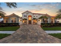 Stunning Mediterranean-style home with lush landscaping, brick driveway, and a beautiful sunset backdrop at 8476 Dunham Station Dr, Tampa, FL 33647