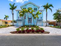 Stunning three-story light blue home featuring lush landscaping and a paver driveway at 11260 7Th E St, Treasure Island, FL 33706