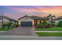 Charming single-story home featuring a tile roof, paved driveway, and lush tropical landscaping at dusk at 20828 Cattail Blvd, Venice, FL 34292