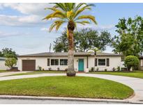 Charming ranch-style home with a circular driveway and a lush green lawn with a bright blue front door at 5934 51St N Ave, Kenneth City, FL 33709