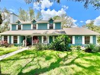 Charming teal two-story home with white trim, dormers, and a lovely front yard landscape at 8834 Whispering Oaks Trl, New Port Richey, FL 34654