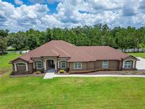 Stunning single-story home featuring a lush green lawn, complemented by mature trees and meticulously maintained landscaping at 13102 Done Groven Dr, Dover, FL 33527